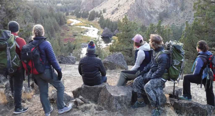 a group of people stand and sit high above a river as they survey it